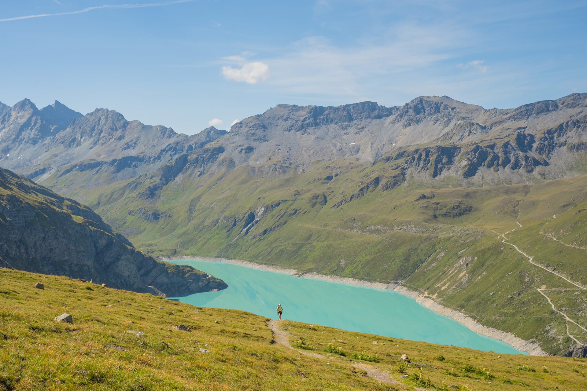 Hiker on mountain trail overlooking turquoise alpine lake and rocky peaks