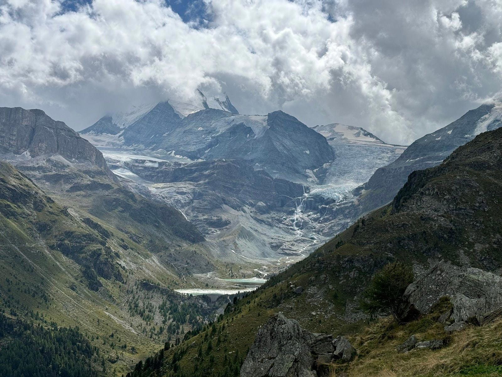 Alpine mountain valley with glacier and snow-capped peaks under cloudy sky