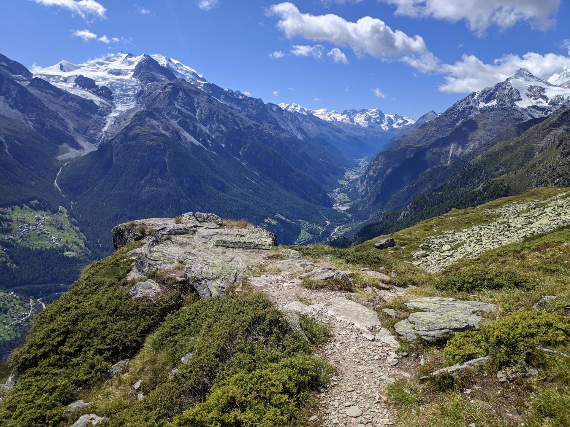 Hiking trail overlooking alpine mountain peaks and valley with snow and glaciers