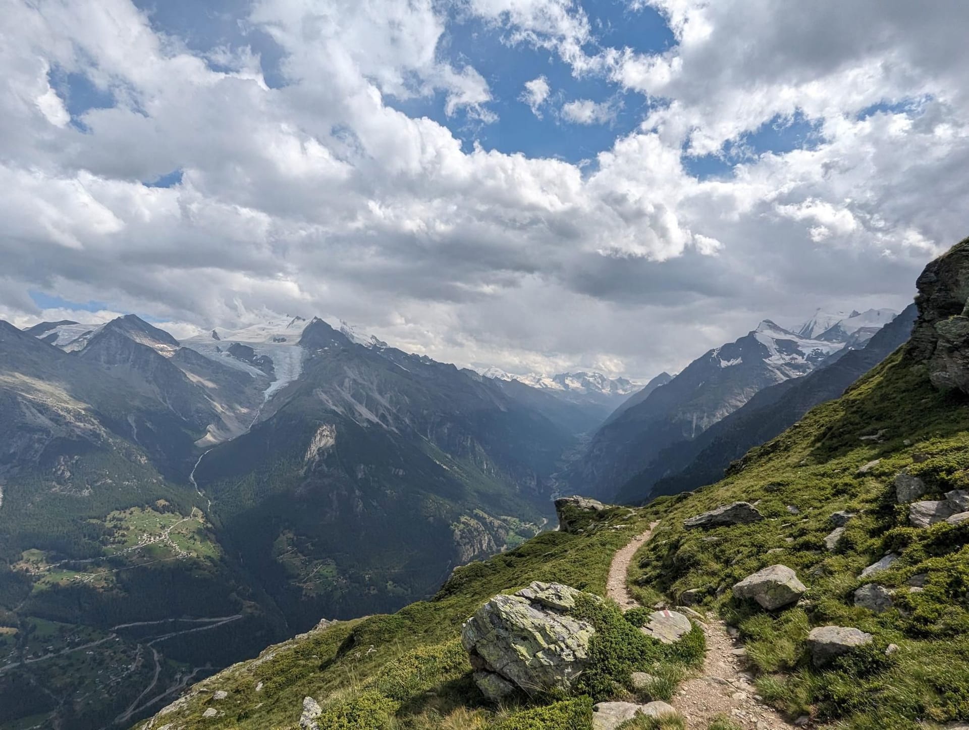 Hiking trail winding through alpine mountain landscape with snowy peaks and cloudy sky