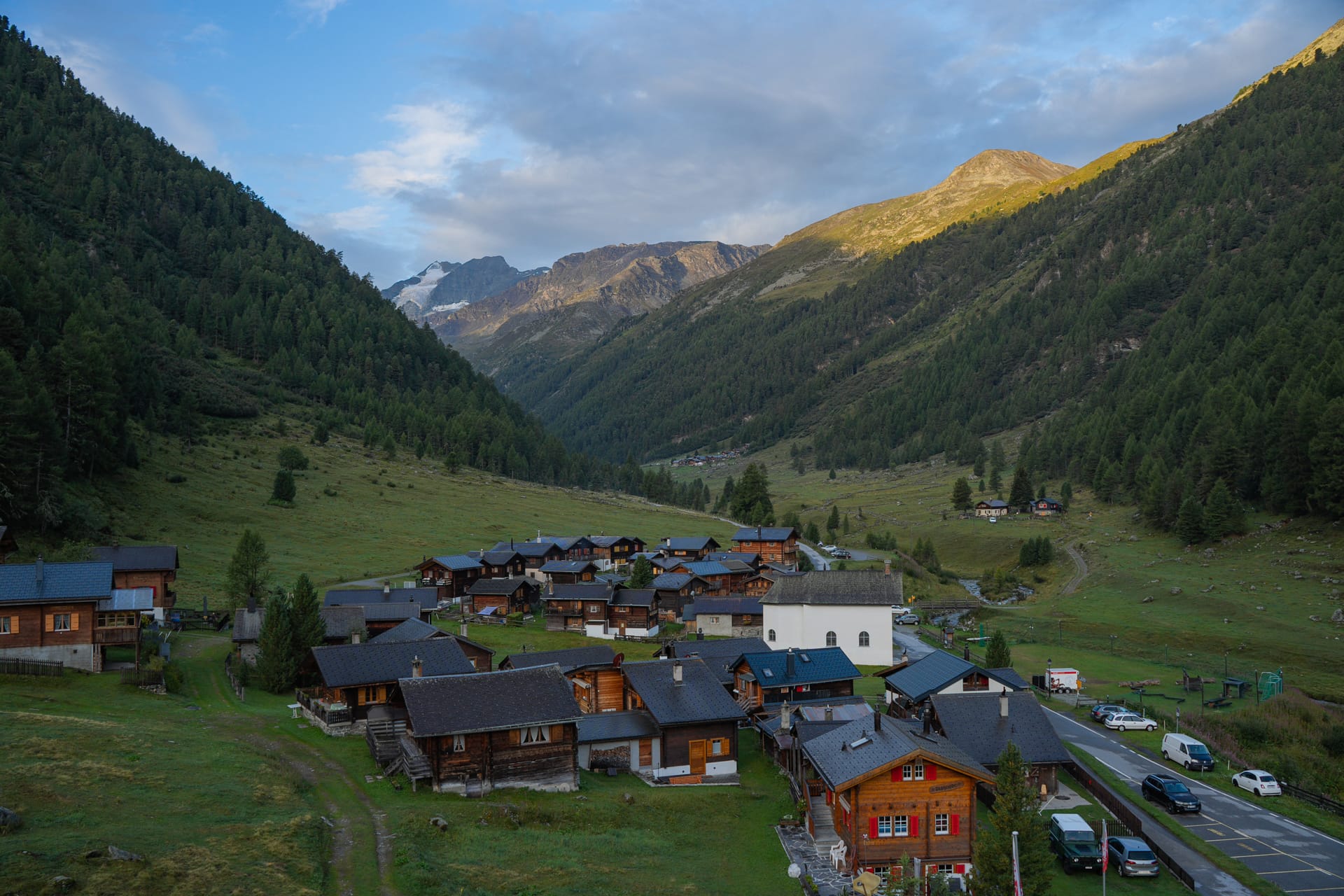 Alpine village with wooden houses nestled in a mountain valley surrounded by pine forests and peaks