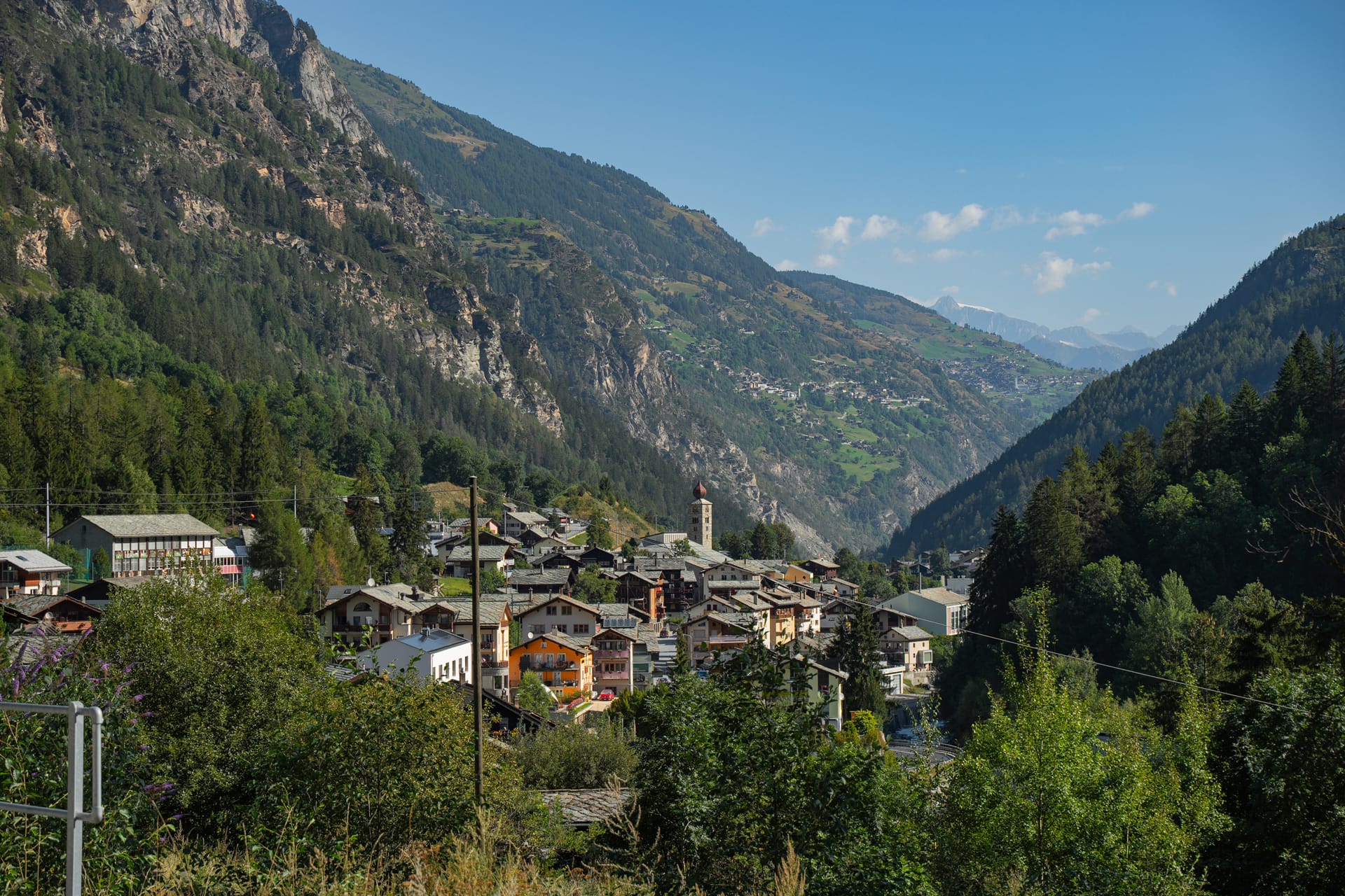 Alpine village nestled in a mountain valley with steep forested slopes and clear blue sky