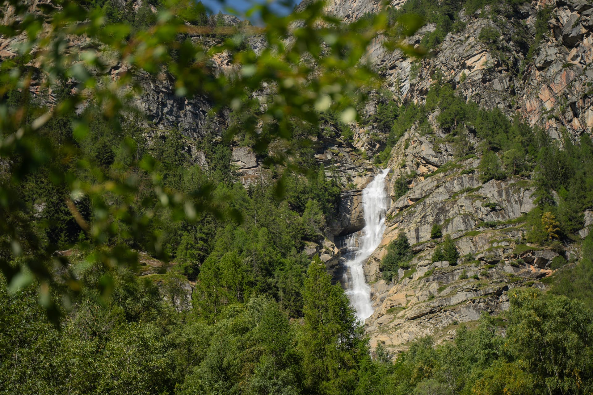 Waterfall cascading down a steep rocky mountain cliff surrounded by green trees