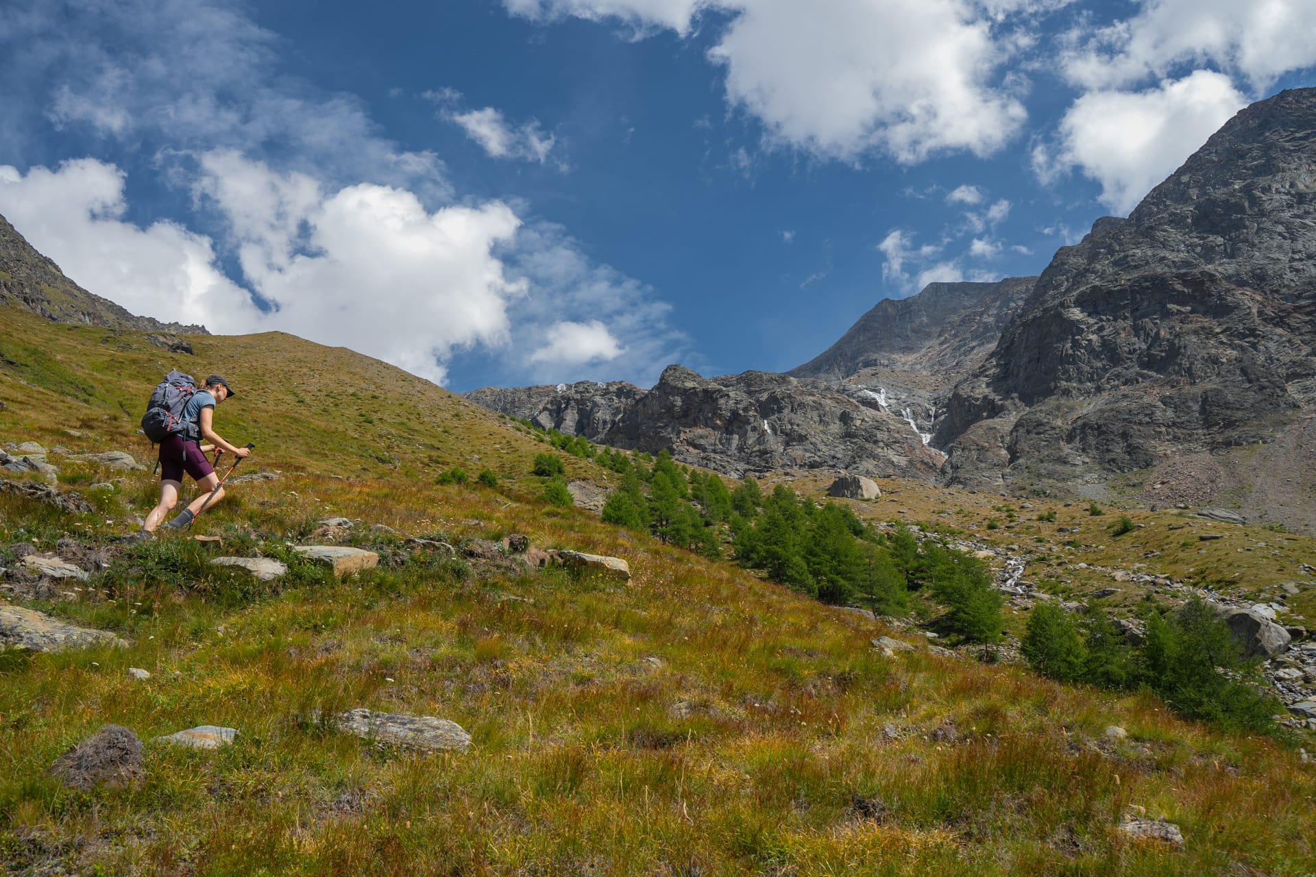 Hiker with backpack and poles walking up alpine mountain trail