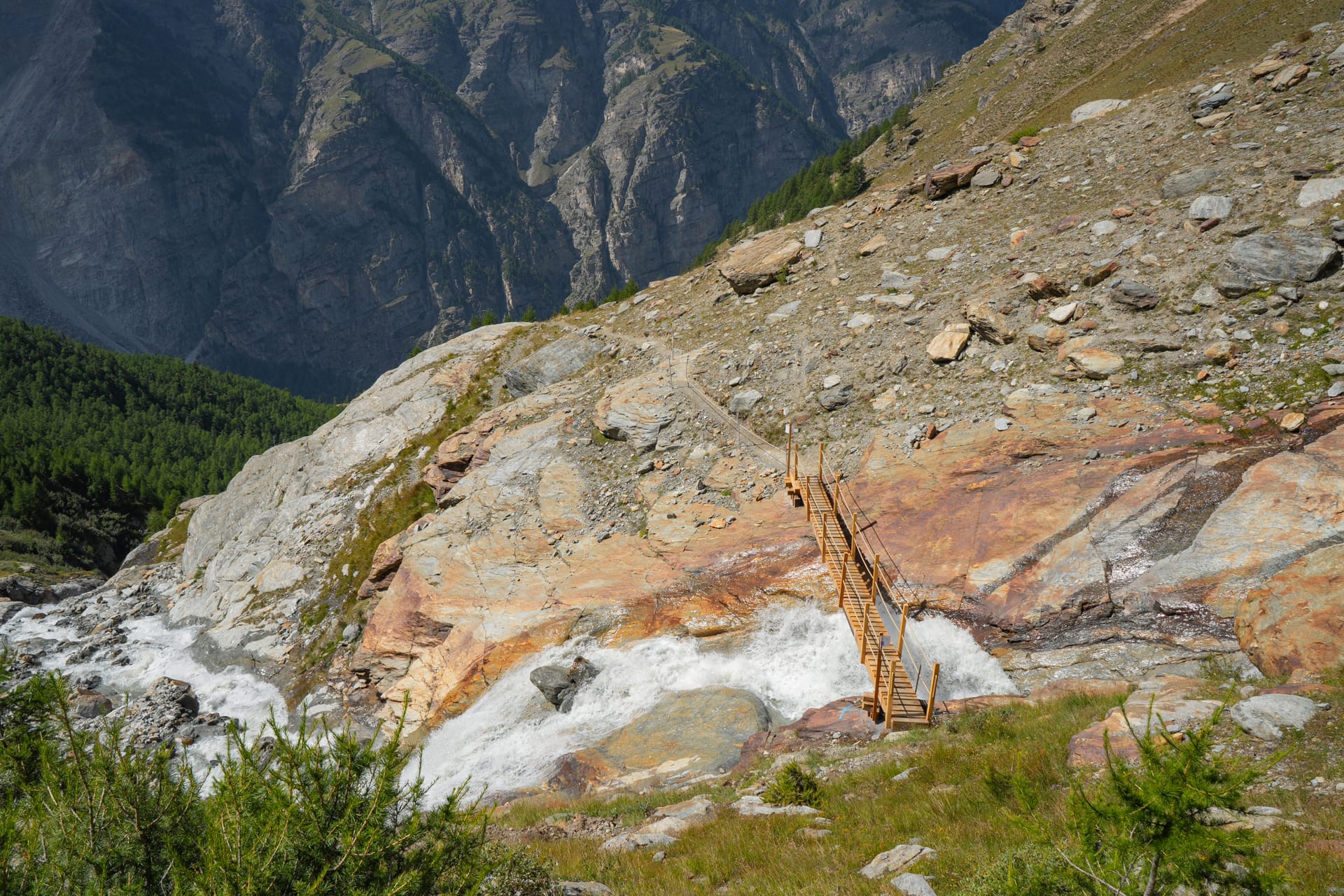 Wooden suspension bridge over mountain waterfall and rocky terrain with hiking trail