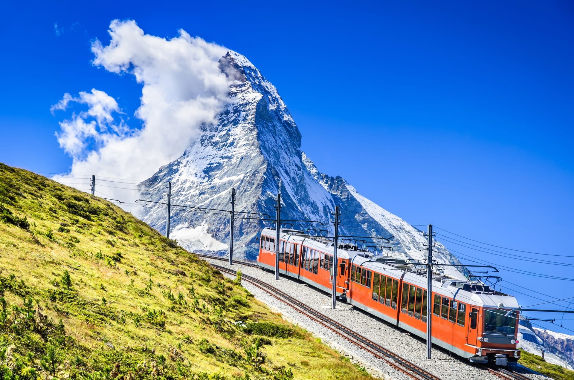 Gornergrat red mountain train climbing alpine slope with Matterhorn peak in background near Zermatt