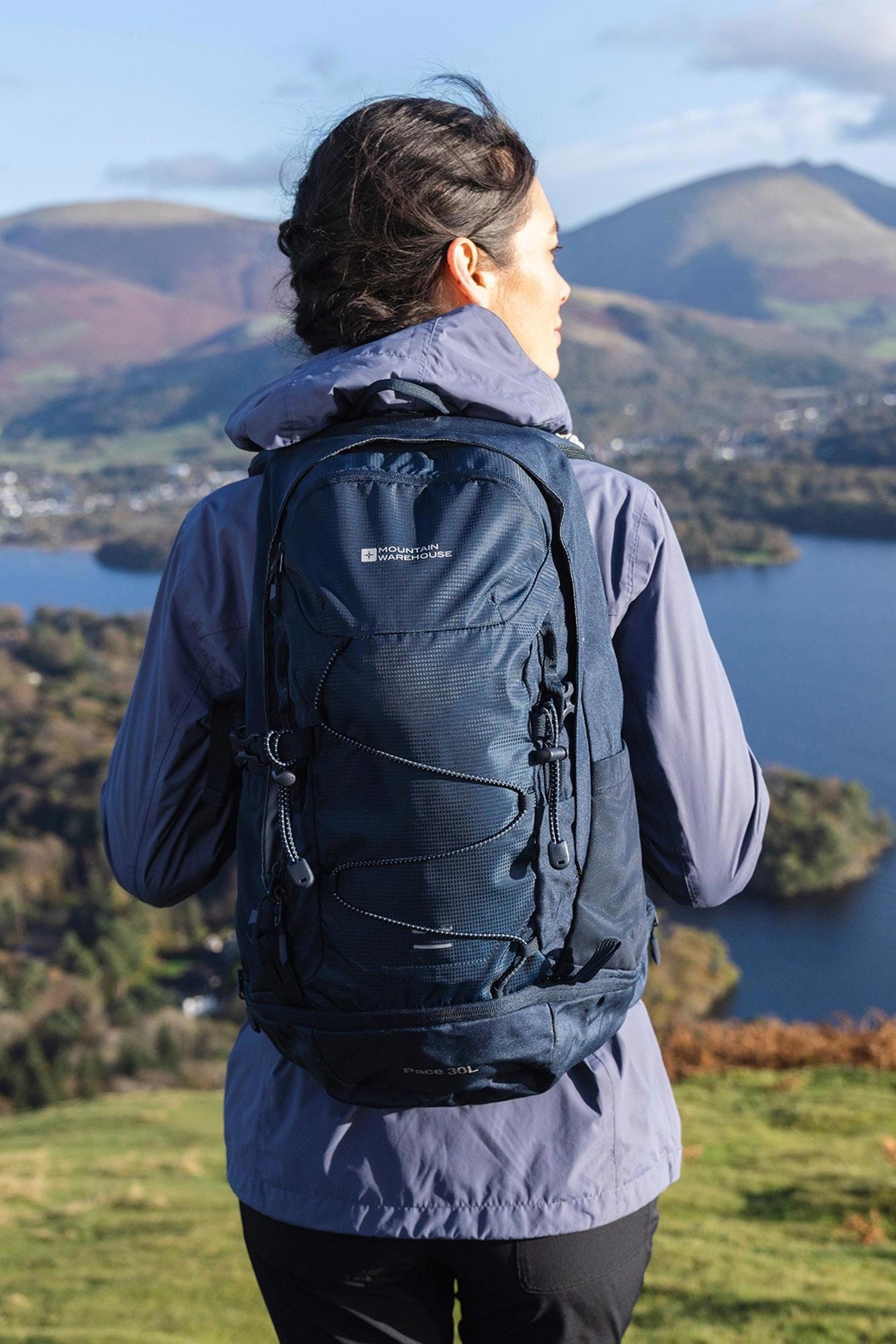 Hiker wearing a blue backpack with mountains and lake in the background