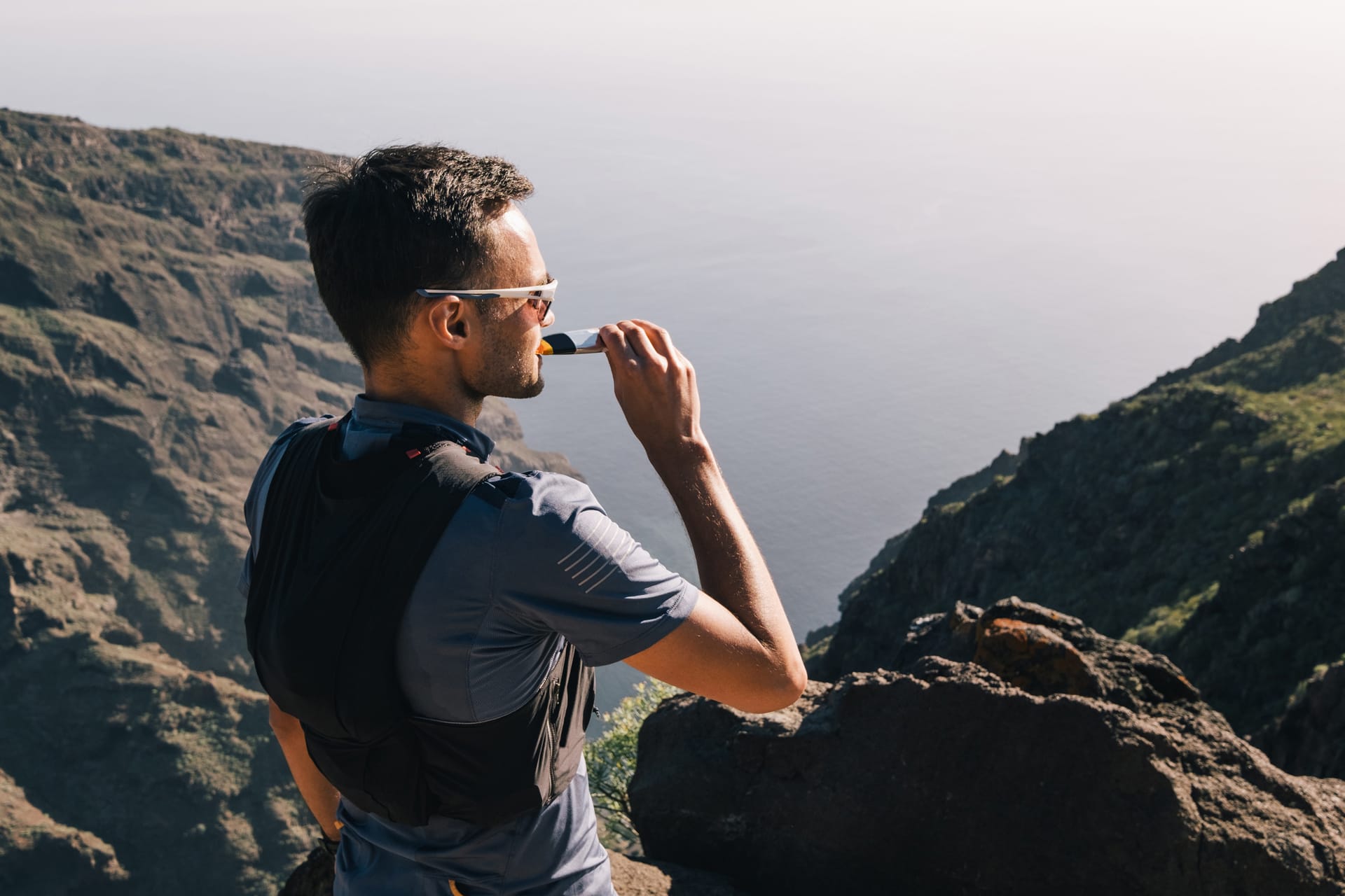 Hiker consuming energy gel on mountain overlook above water
