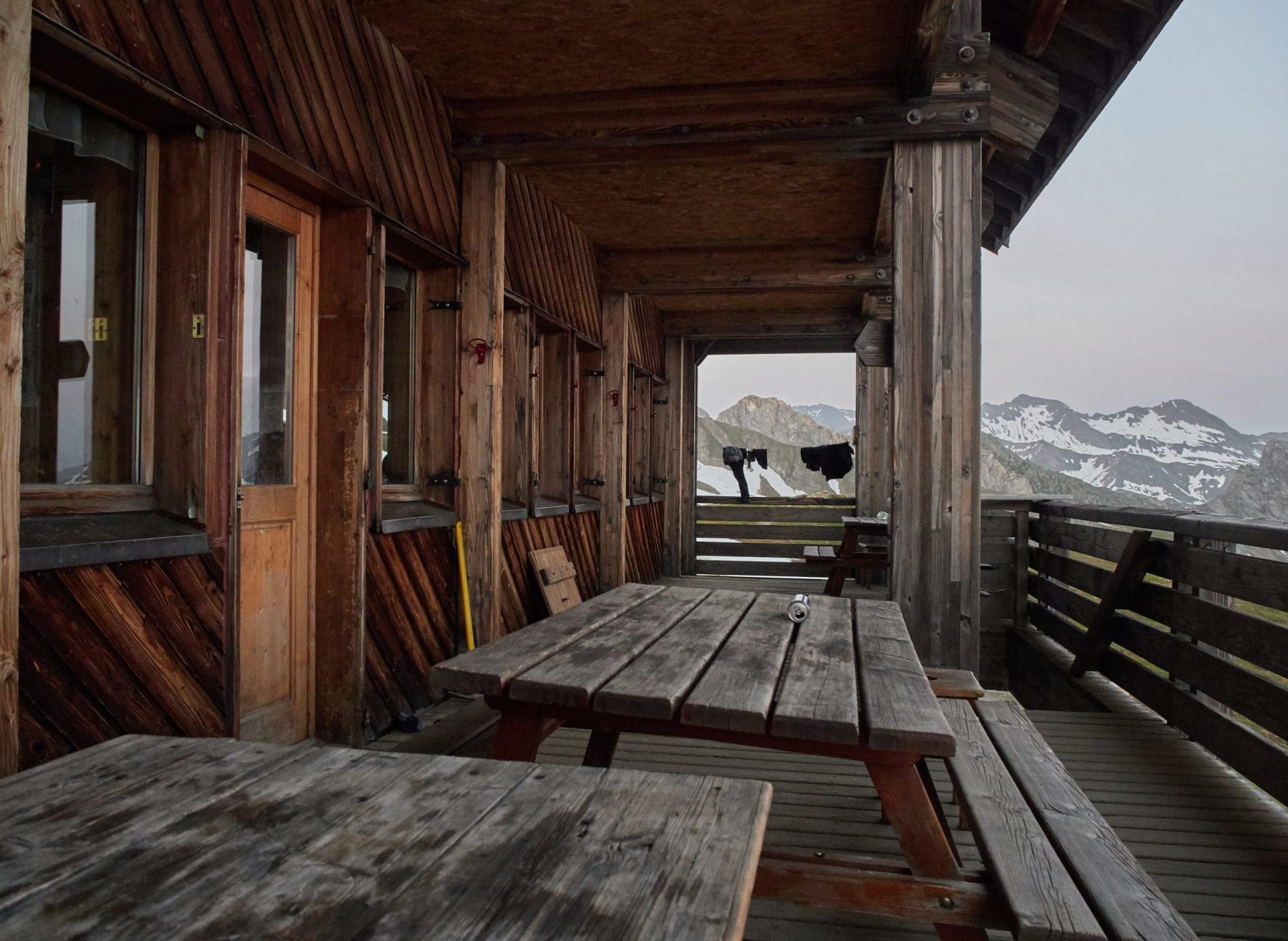 Wooden picnic tables on the covered porch of an alpine mountain hut overlooking snowy peaks