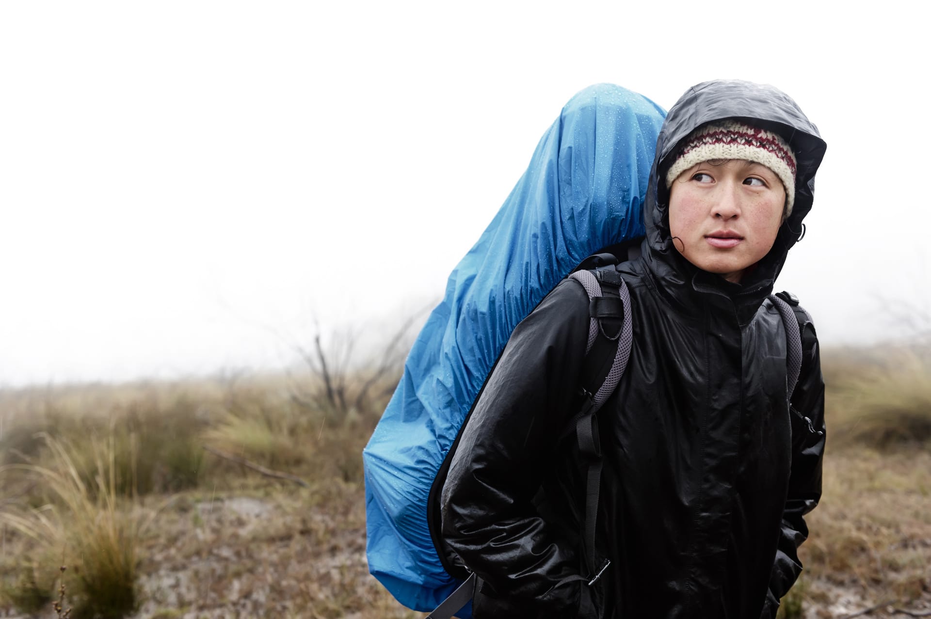 Hiker wearing a black waterproof jacket and backpack with blue cover in foggy outdoor setting
