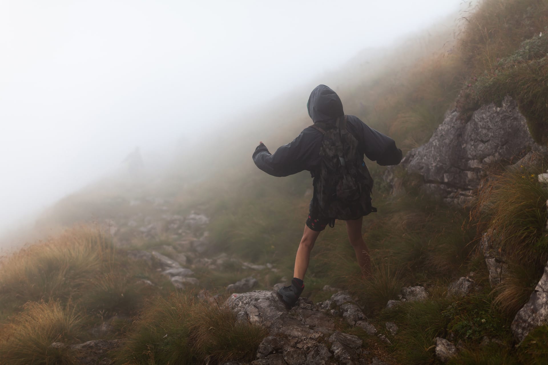 Hiker wearing a hooded rain jacket on a foggy mountain trail
