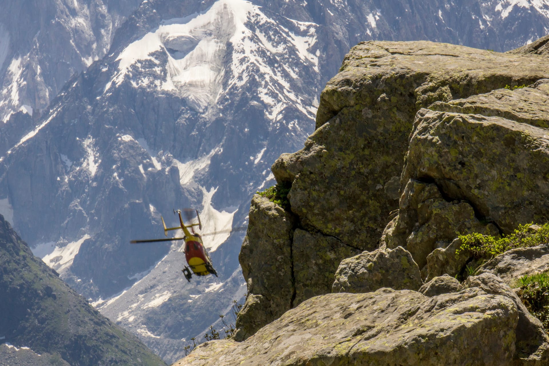 Rescue helicopter flying near rocky alpine mountain peaks with snow