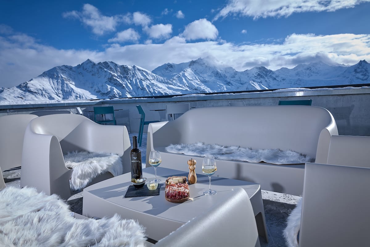 Outdoor terrace dining with wine and food against snowy alpine mountain peaks