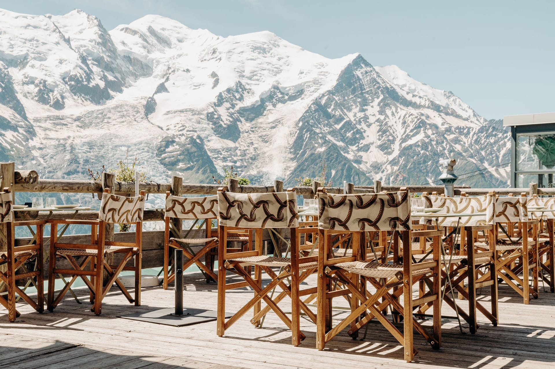Outdoor restaurant terrace with wooden chairs and tables overlooking snow-capped mountain peaks