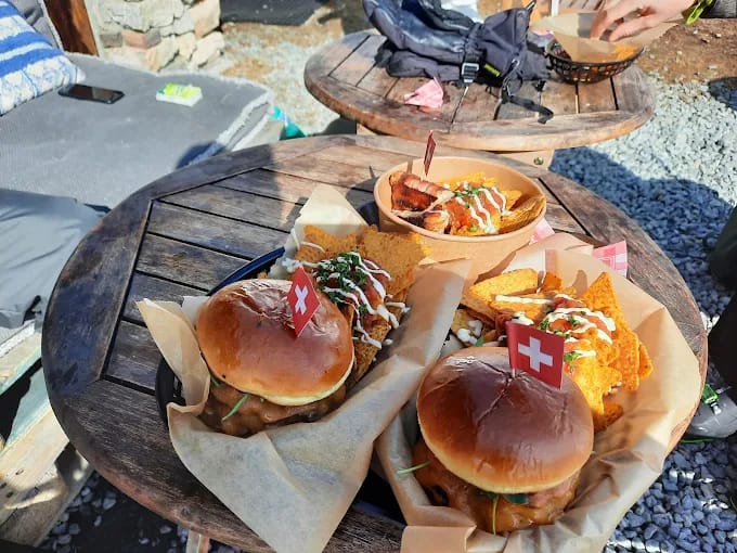 Burgers and nachos served with Swiss flags on wooden outdoor tables in Arolla