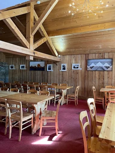 Wooden dining tables and chairs inside rustic room with exposed wooden beams and paneled walls