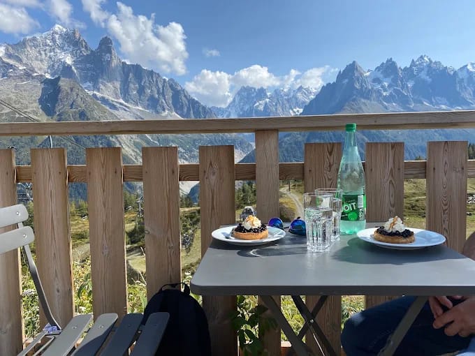 Outdoor table with pastries and drinks on a balcony overlooking snowy mountain peaks