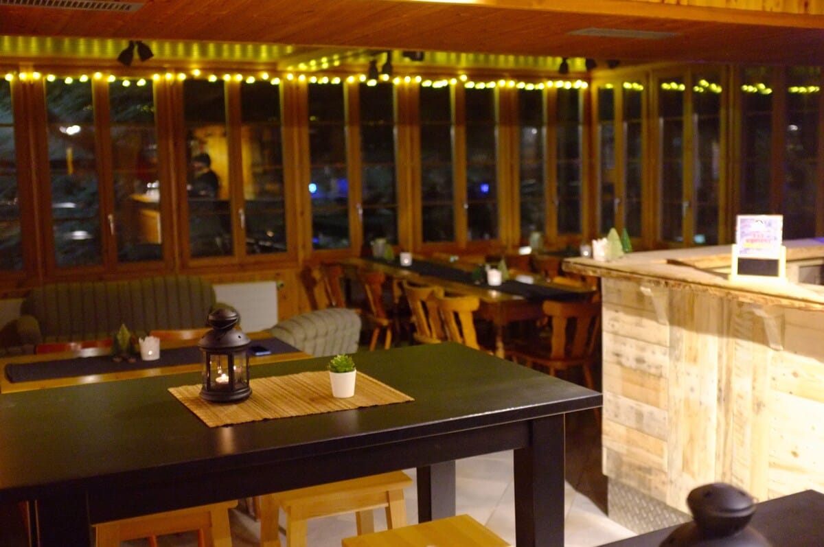 Cozy rustic interior of Pension Du Lac Bleu with wooden tables, string lights, and lantern