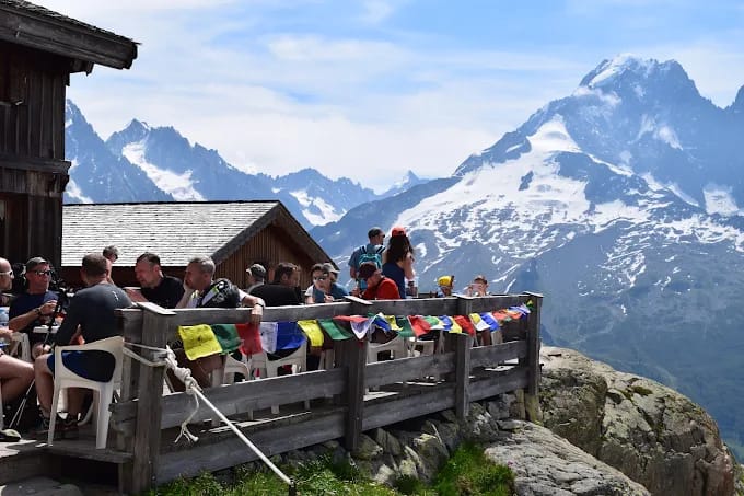 People dining on outdoor wooden terrace with alpine mountain peaks and snow
