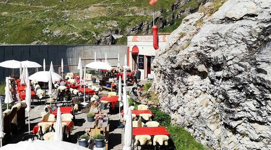 Outdoor restaurant terrace with red tables and white umbrellas near a rocky mountain cliff