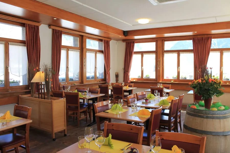 Restaurant interior with wooden tables, chairs, and large windows with red curtains