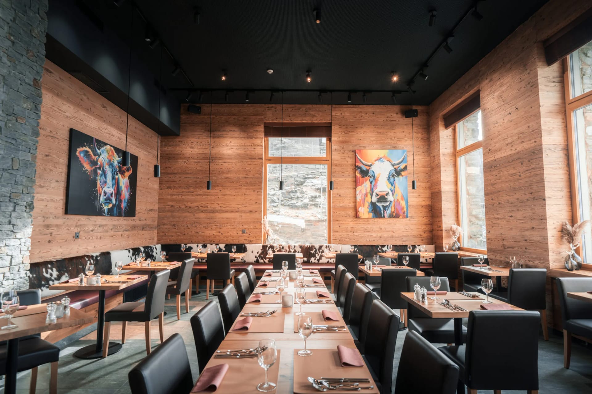 Restaurant interior with wood-paneled walls, black chairs, and colorful cow paintings