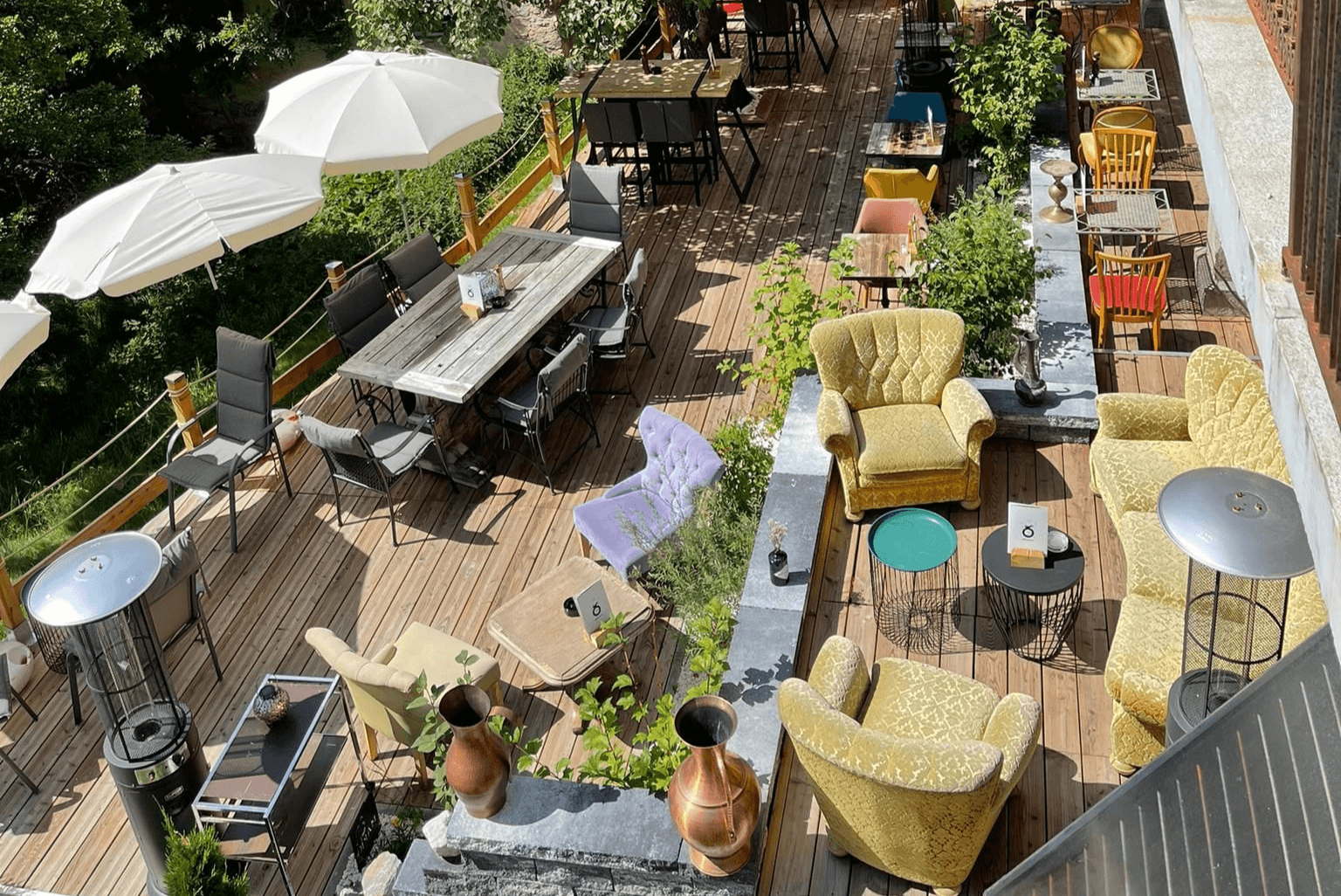 Outdoor wooden terrace dining area with armchairs, tables, and white umbrellas