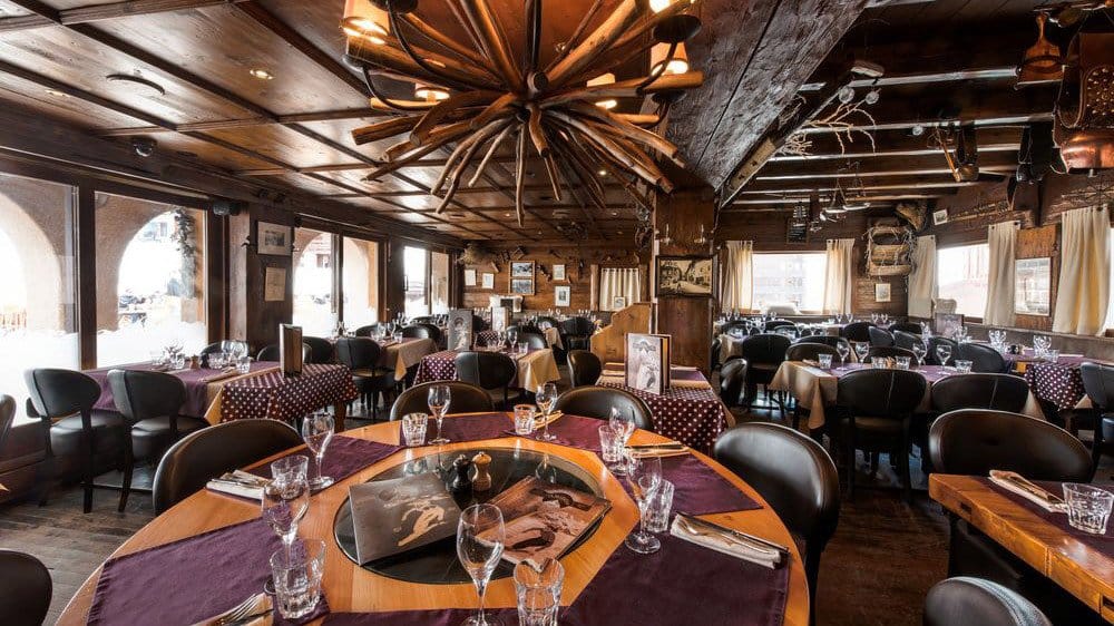 Rustic restaurant interior with wooden walls, ceiling beams, and tables set with purple placemats and wine glasses