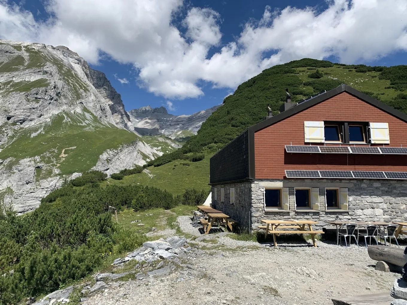 Ringelspitzhütte mountain hut with picnic tables against steep green and rocky alpine slopes.