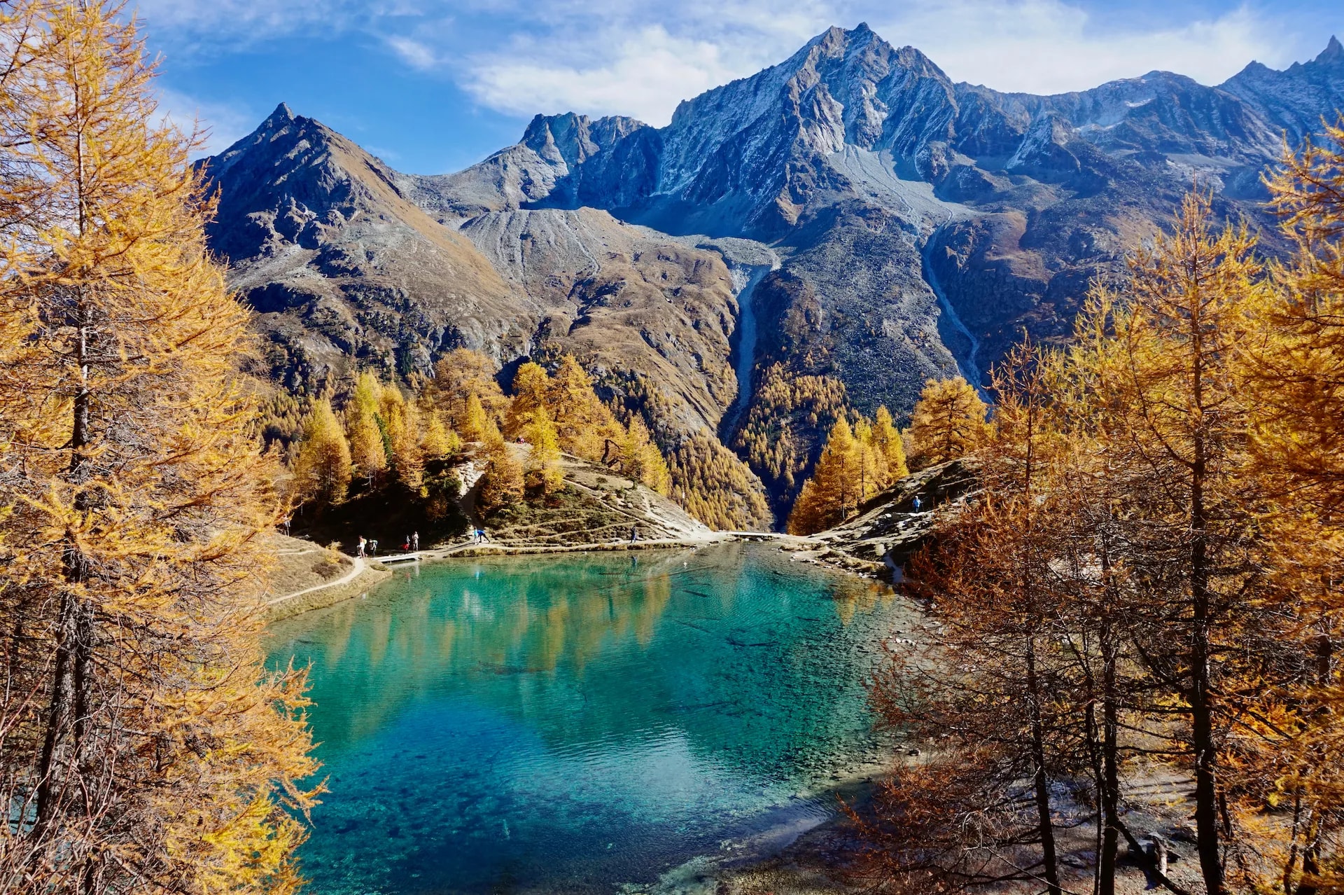 Lac Bleu Arolla with turquoise water, autumn larches, and rugged alpine mountains.