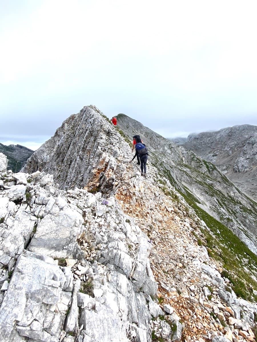 Hikers traversing a rocky mountain ridge under an overcast sky.