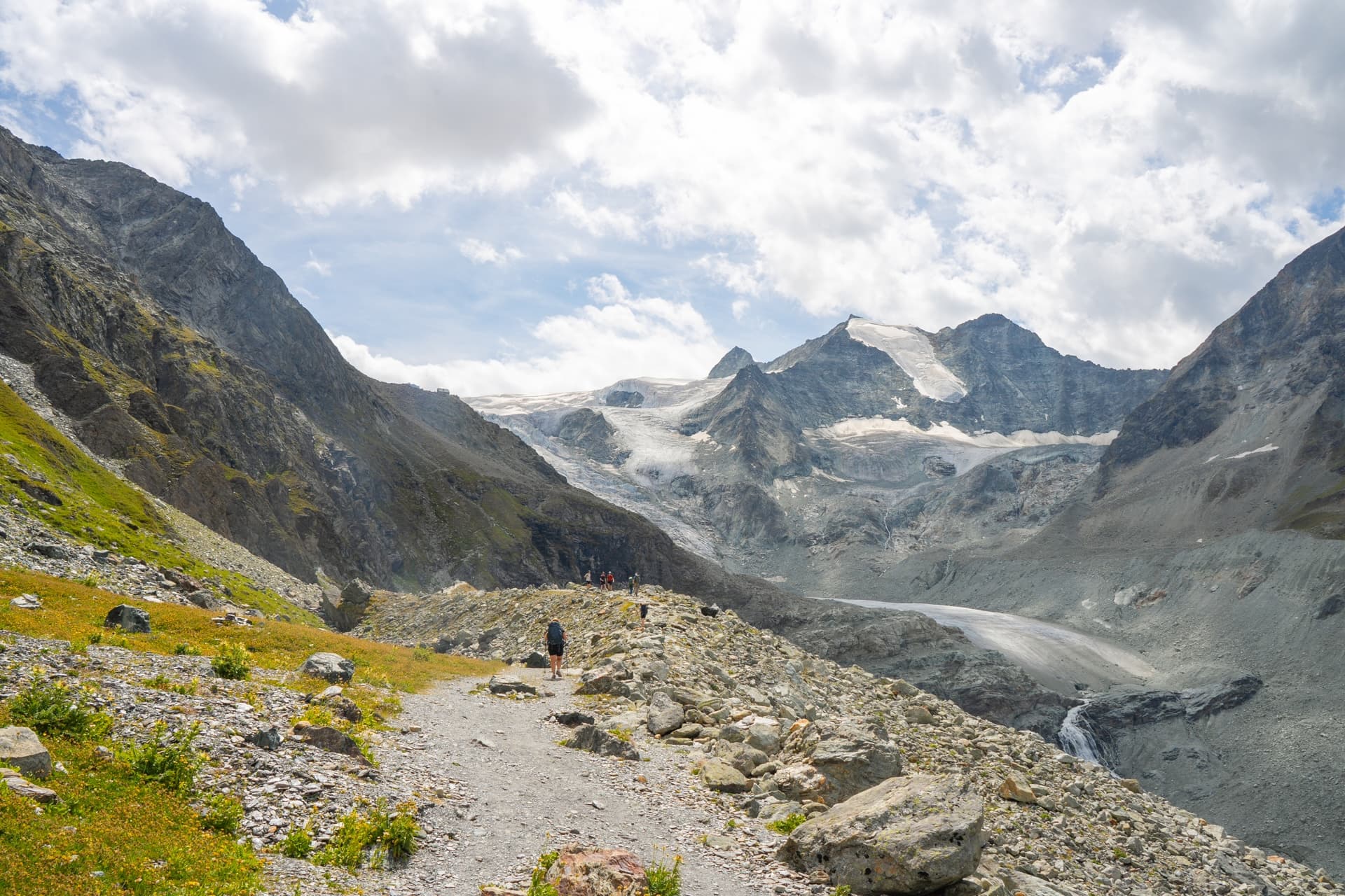 Hikers on rocky trail approaching glacier terminus above Lac de Moiry.