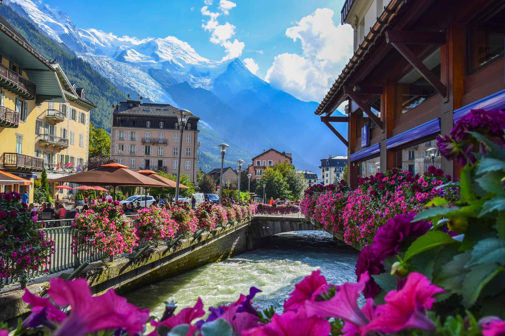 Chamonix town center with river, buildings, and snow-capped mountains in background.