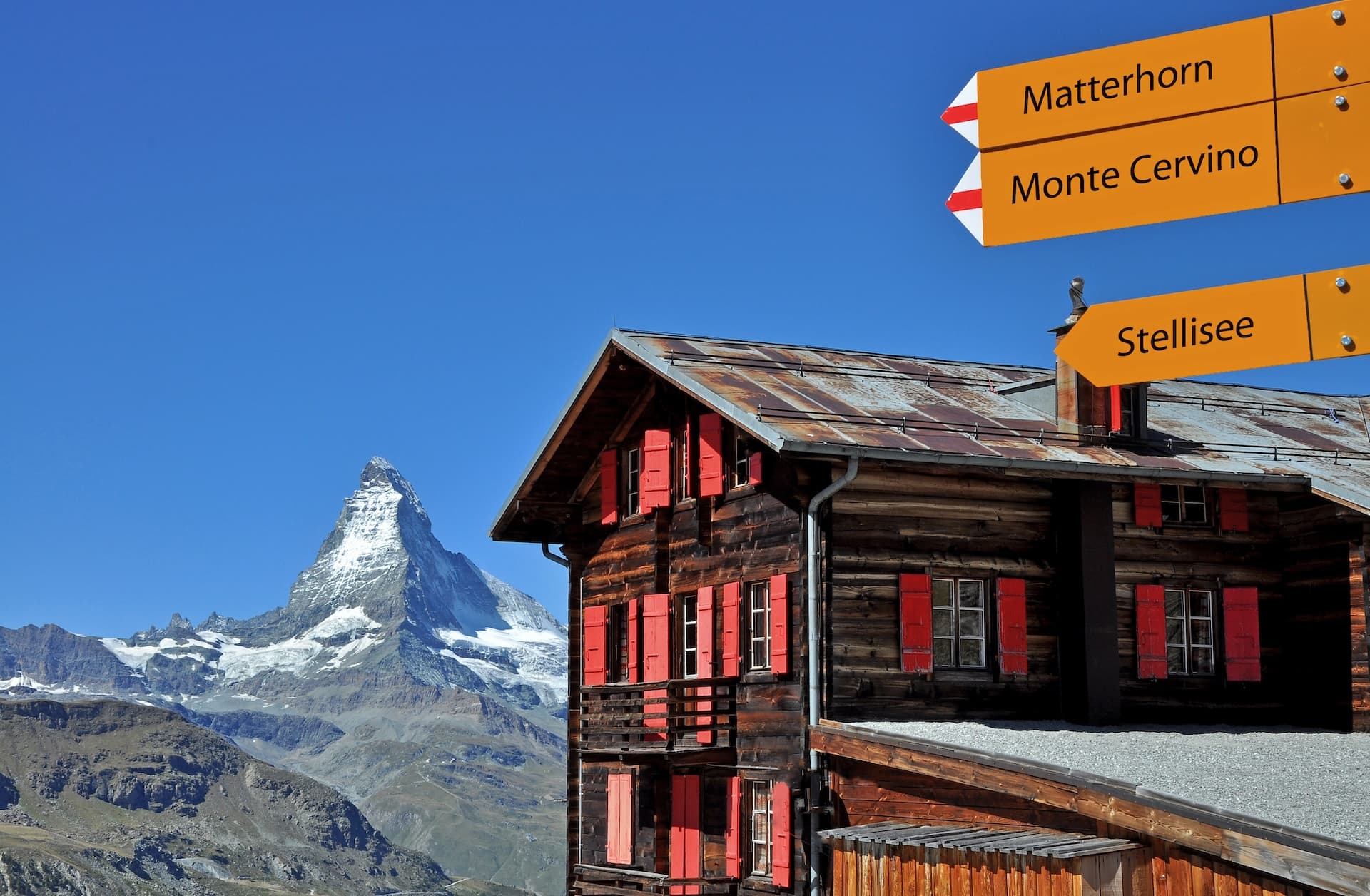 Alpine hut with red shutters, Matterhorn, and hiking signs for Stellisee.