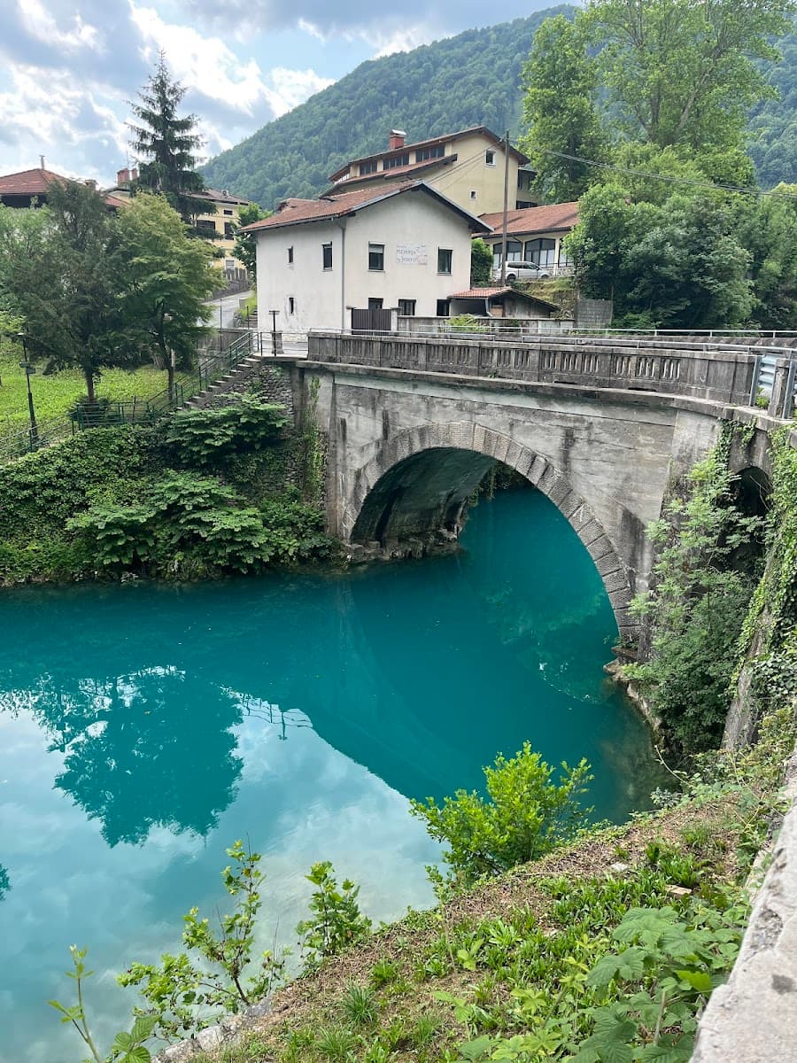 Stone bridge over turquoise river with buildings and lush green mountainsides