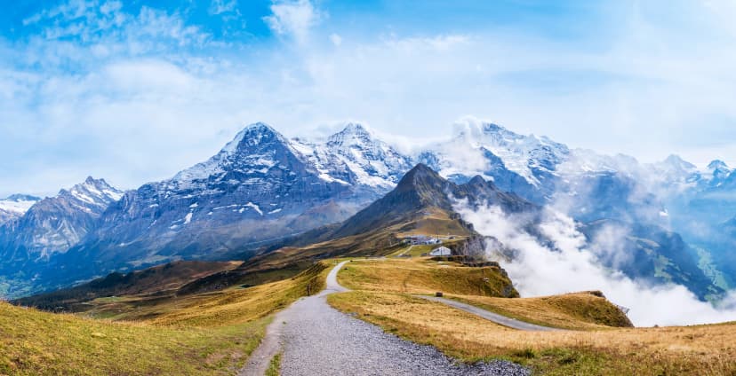 Autumn in Swiss Alps. Hiking trail on top of Mannlichen near Wengen and Lauterbrunnen, Switzerland. Mountain range with peaks Eiger, Monch, Jungfraujoch and Jungfrau in clouds. Grindelwald valley