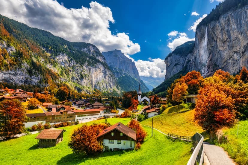 Captivating autumn view of Lauterbrunnen valley with gorgeous Staubbach waterfall and Swiss Alps at sunset time. Lauterbrunnen village with autumn red foliage, Berner Oberland, Switzerland, Europe.