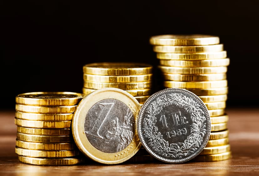 one euro coin and one swiss frank and gold money on the desk