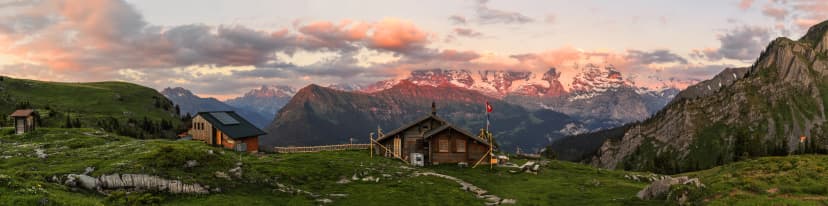 Panorama of Swiss alps on high altitude with mountains huts for trekker with the background of Eiger, Monch and Jungfrau peaks in the golden sunset hours