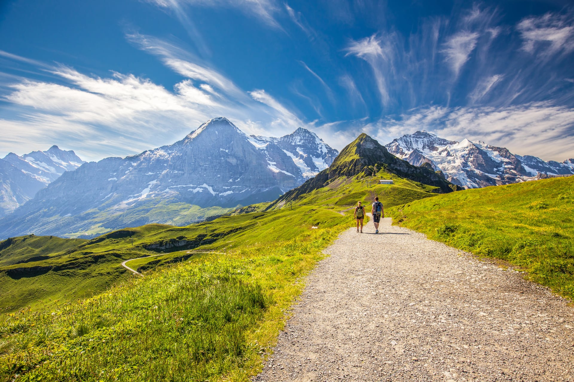 Young couple hiking in panorama trail leading to Kleine Scheidegg from Mannlichen with Eiger, Monch and Jungfrau mountain (Swiss Alps) in the background, Berner Oberland, Grindelwald, Switzerland.