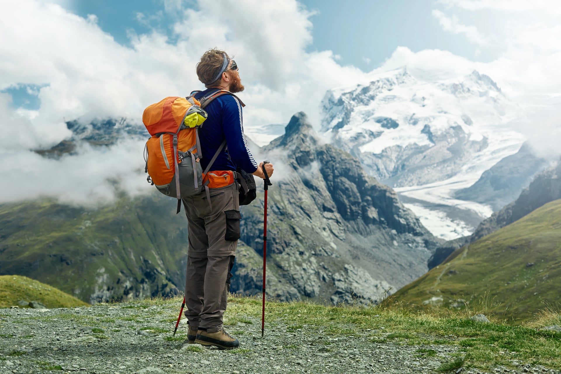 hiker with backpack stands on the trail in the Apls mountains. Trek near Matterhorn mount. Mountain ridge and blue sky on the background