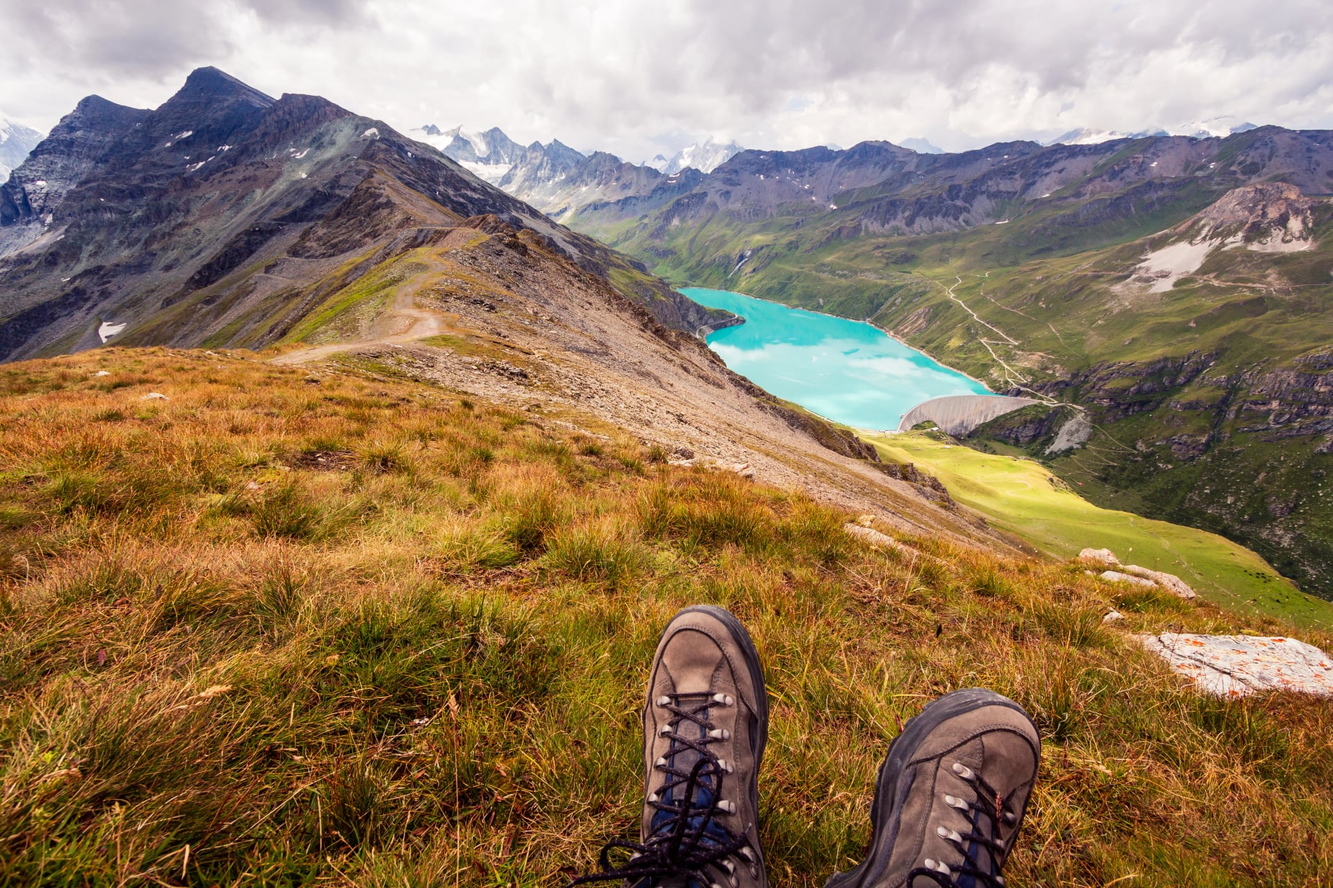Enjoy breathtaking view from the top of a mountain on a mountain lake. First person perspective of hiking shoes. Corne de Sorebois, Grimentz, Valais, Switzerland