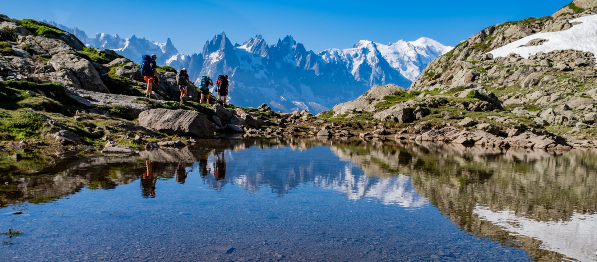 Reflektion av vandrare i en alpin sjö på Tour Du Mont Blanc