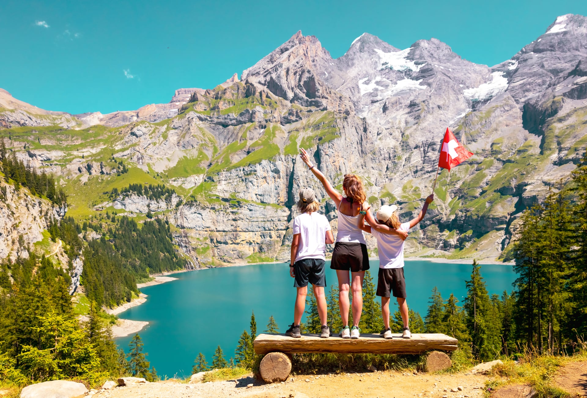 Famille heureuse en Suisse - montagnes des Alpes et lac bleu avec mère et fils tenant le drapeau suisse - voyage, tourisme, aventure