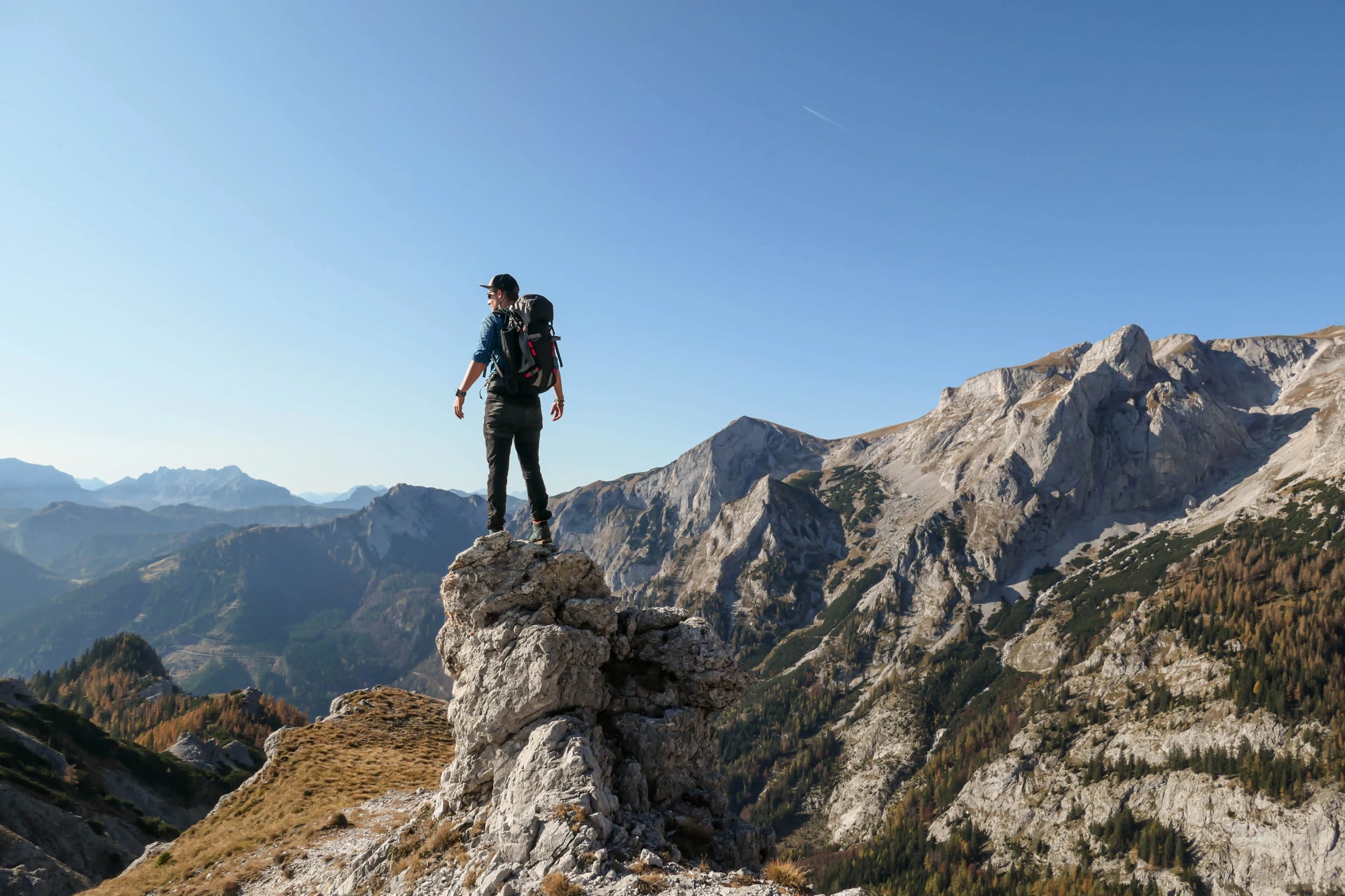 En man som står på toppen av en skarp, spetsig sten i Hochschwab-regionen, österrikiska Alperna. Den branta bergsväggen framför ser mycket farlig ut. Hög bergsklättring. Höstvibbar. Äventyr och frihet
