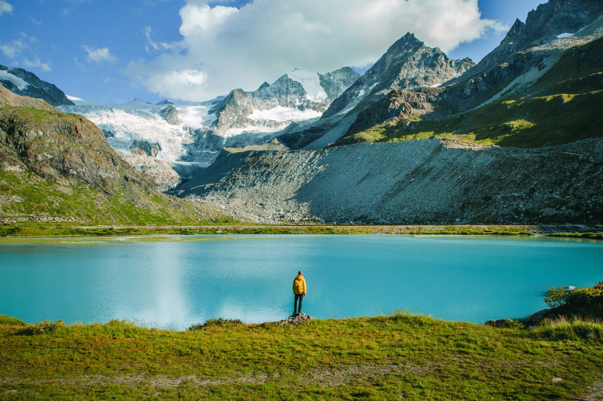A Man In Yellow Jacket Standing Beside Turquoise Lake with Snowy Peaks in Lac de Châteaupré, Switzerland