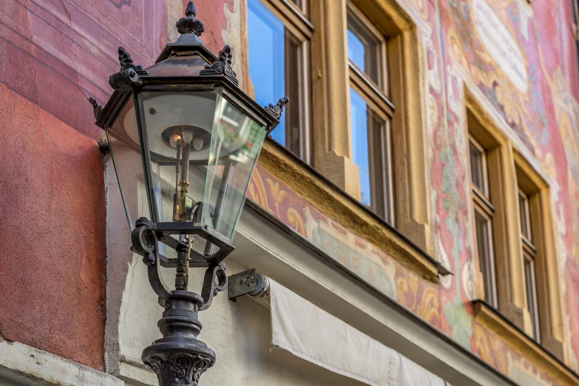 Ornate black metal lantern mounted on a building facade with colorful frescoes and windows.