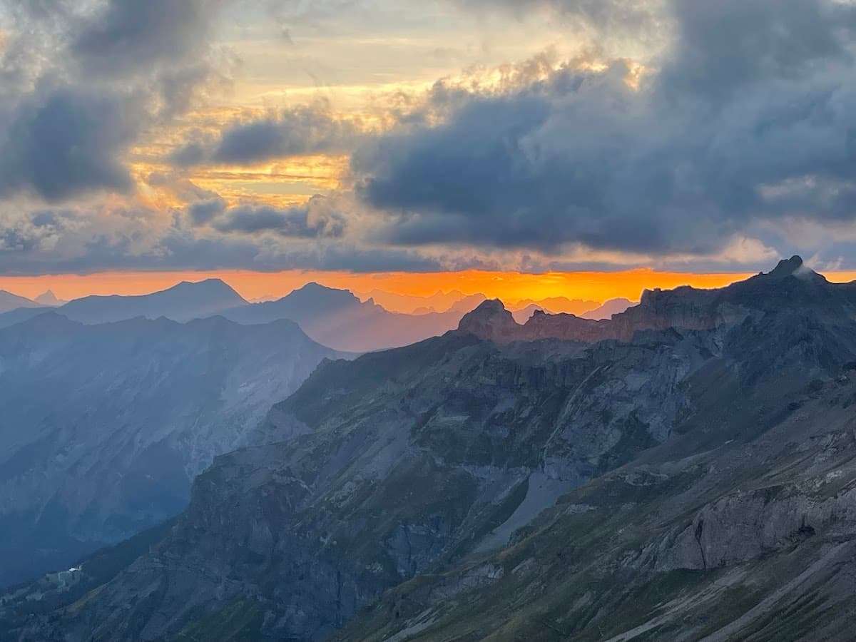 Mountain peaks at sunset with dramatic clouds and glowing orange horizon