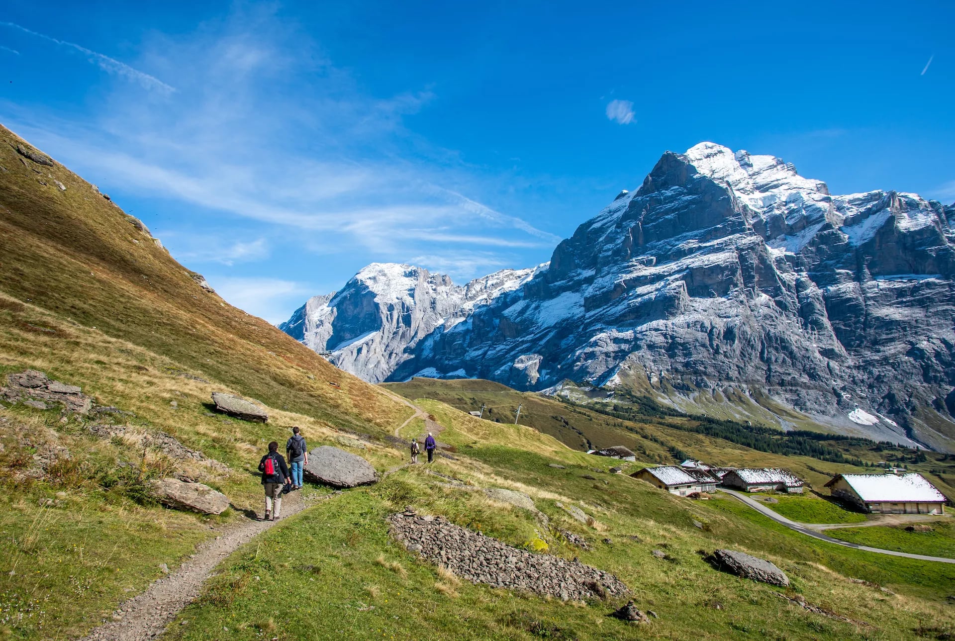 Hikers on path near Grosse Scheidegg above Grindelwald with snow-capped mountains.