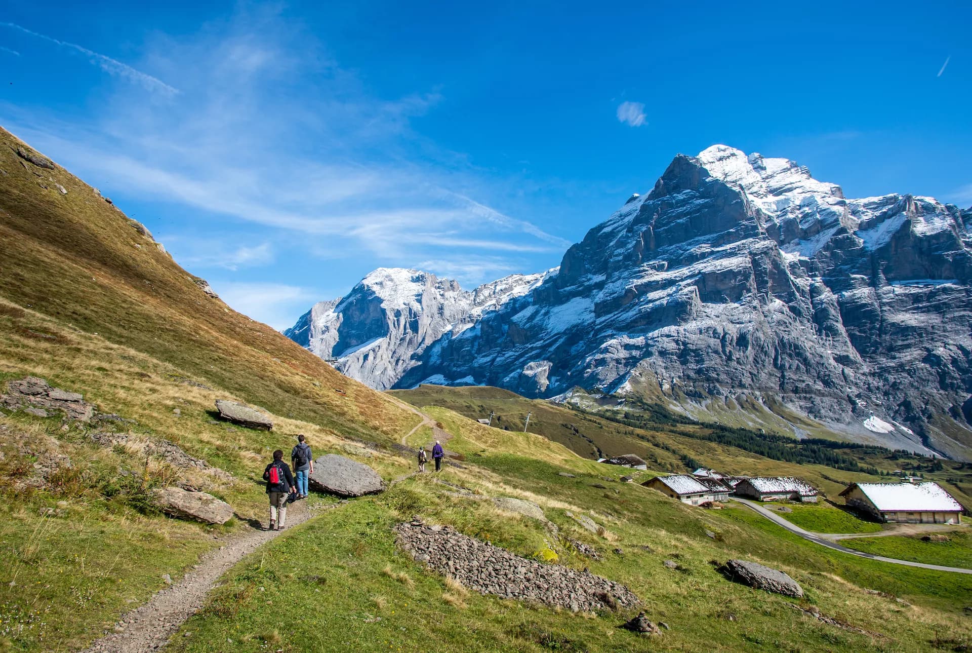 Hikers on path near Grosse Scheidegg above Grindelwald with snow-capped mountains.